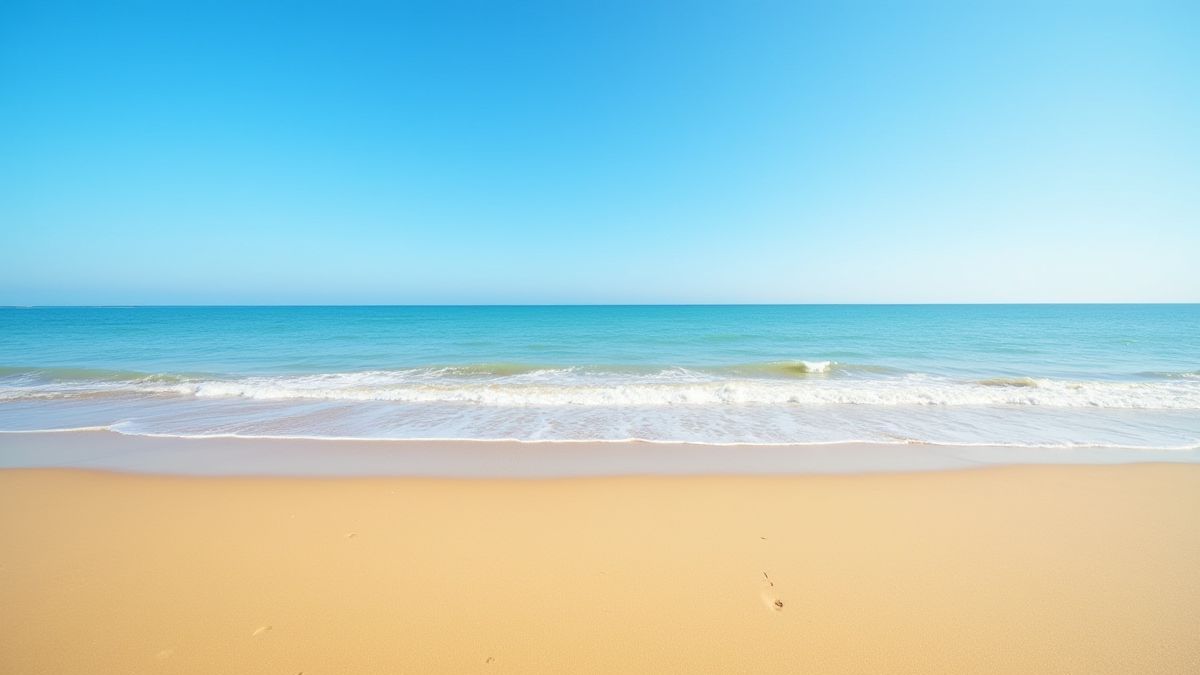 A tranquil beach with golden sand and soft waves under a clear blue sky.