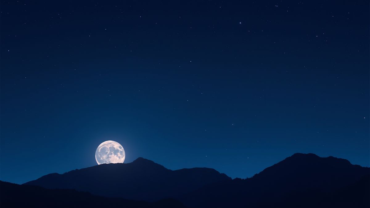 Cielo estrellado con luna llena y siluetas de picos montañosos.